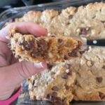Lactation Cookie Bar held in front of the pan with the rest of the peanut butter chocolate chip lactation bars