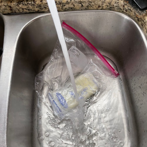 frozen bag of breast milk in a sink with hot water running on top of it