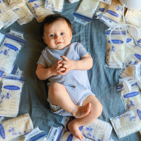 Pumping photoshoot: Baby laying on a blue sheet with bags of breastmilk surrounding baby