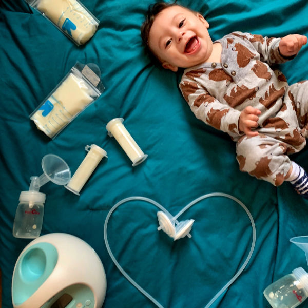 Exclusive Pumping Photoshoot: Baby on a green background with bottles and bags of breastmilk and a Spectra pump with the tubing in the shape of a heart