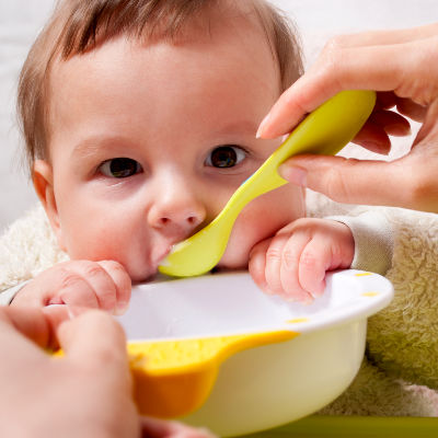 Solids and Breast Milk: Baby eating solid food from a yellow bowl in a spoon
