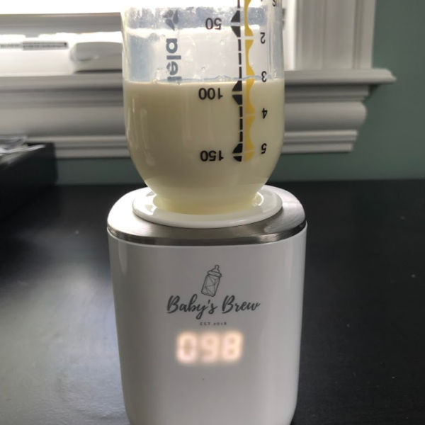 Baby's Brew breast pump on a black desk, warming about 3 oz of breast milk. The timer is on showing how much longer the milk has to warm.
