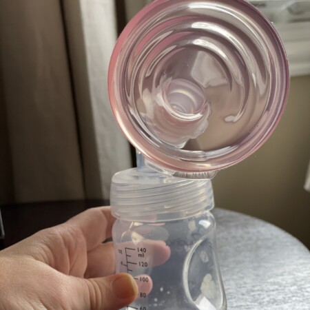 Pink silicone Pumpin Pals attached to a Baby Buddha bottle held up by a hand with a brown table in the background