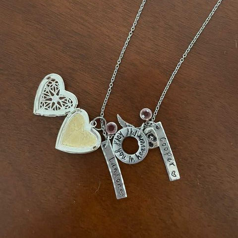 Breastmilk locket necklace in a heart shape with the names Cooper and Landon engraved on a brown table background