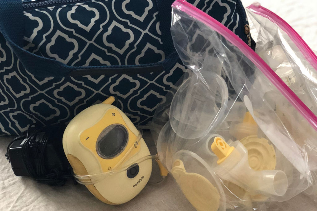Medela breast pump in front of a breast pump bag with packed up pump parts