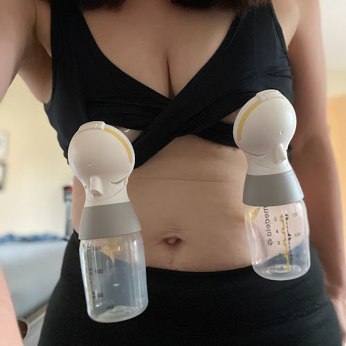 woman wearing black Larken X hands-free pumping bra with Medela pump parts set up. Only her chest and belly are shown.