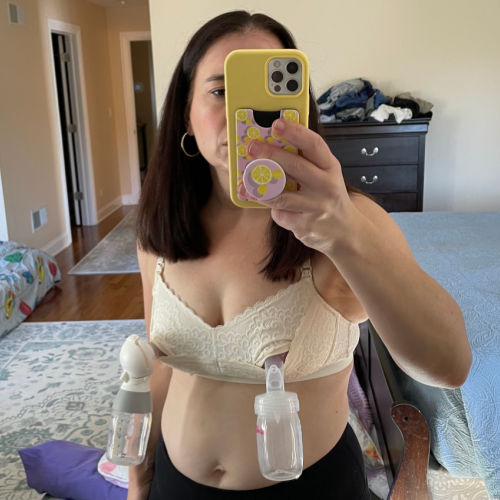 Woman wearing cream Dairy Fairy Pippa hands-free pumping bra set up for pumping. She's taking her picture in the mirror.