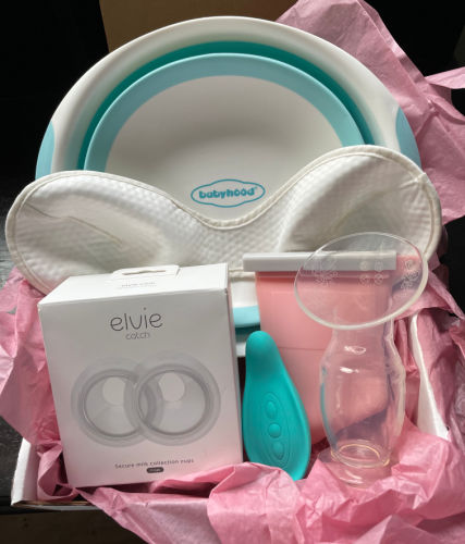 a box with pink tissue paper containing an Elvie Curve, a Haakaa, a Lavie lactation massager, a pink Junobie bag, a davin & adley bra liner, and a wash basin 