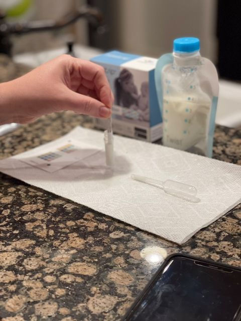 Woman dipping a test strip into a tube full of breast milk with a Kiinde breast milk bag in the background