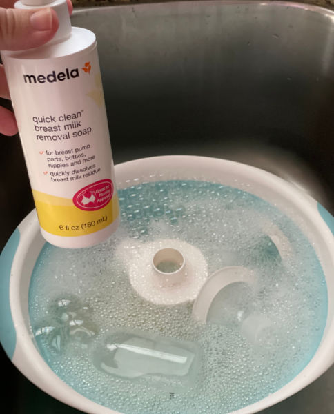 Medela breast pump parts in a blue wash basin with a bottle breast milk removal soap held in the foreground
