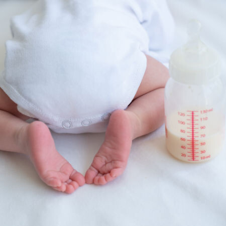 baby wearing white onesie with half full bottle of milk