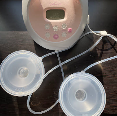 A Spectra S2 breast pump connected to Legendairy Milk Silicone Collection cups on a black surface