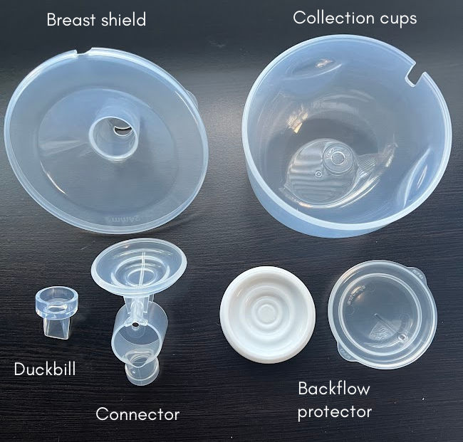 Cara cup breast pump parts laid out on a black desk with text overlay labeling each part - breast shield, collection cups, duckbill, connector, backflow protector diaphragm and cap